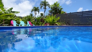 Una piscina blava i cristal·lina amb reflexes, envoltada de vegetació verda i una tanca de fusta.