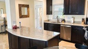 Una cocina moderna con armarios oscuros, encimera de mármol y una mesa de comedor de cristal.