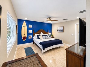 A bedroom with a bed, a ceiling fan, a surfboard decoration, and a beach-themed wall. - Luxury Waterfront Retreat with Private Dock, Golf Cart & Beach Access (Indian Rocks Beach)