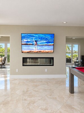 A spacious living area with a large flat-screen TV mounted on the wall, a fireplace below it, and a pool table to the right. - Luxury Waterfront Retreat with Private Dock, Golf Cart & Beach Access (Indian Rocks Beach)