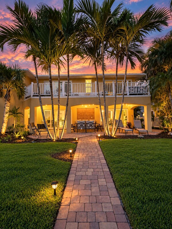 A two-story house with a balcony, a paved pathway, and palm trees. - Luxury Waterfront Retreat with Private Dock, Golf Cart & Beach Access (Indian Rocks Beach)