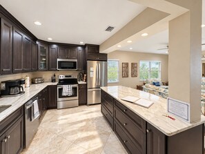 A modern kitchen with dark cabinetry, stainless steel appliances, and a marble countertop. - Luxury Waterfront Retreat with Private Dock, Golf Cart & Beach Access (Indian Rocks Beach)