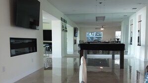 Un amplio salón con una mesa de centro de vidrio, un televisor de pantalla plana en la pared y una cocina al fondo.