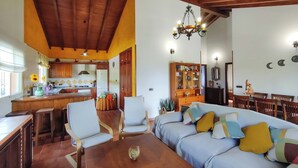 Un'ampia zona giorno con divano, poltrone, tavolo da pranzo, cucina e lampadario.