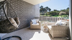 Ein Balkon mit Korbmöbeln, darunter ein Hängesessel und zwei Sofas, einer Ziegelwand und Blick ins Grüne.