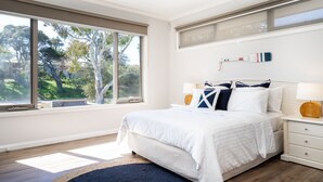 Ein Schlafzimmer mit großem Fenster, einem Bett mit weißer Bettwäsche, einem Deckenventilator und einem Nachttisch mit Lampe.