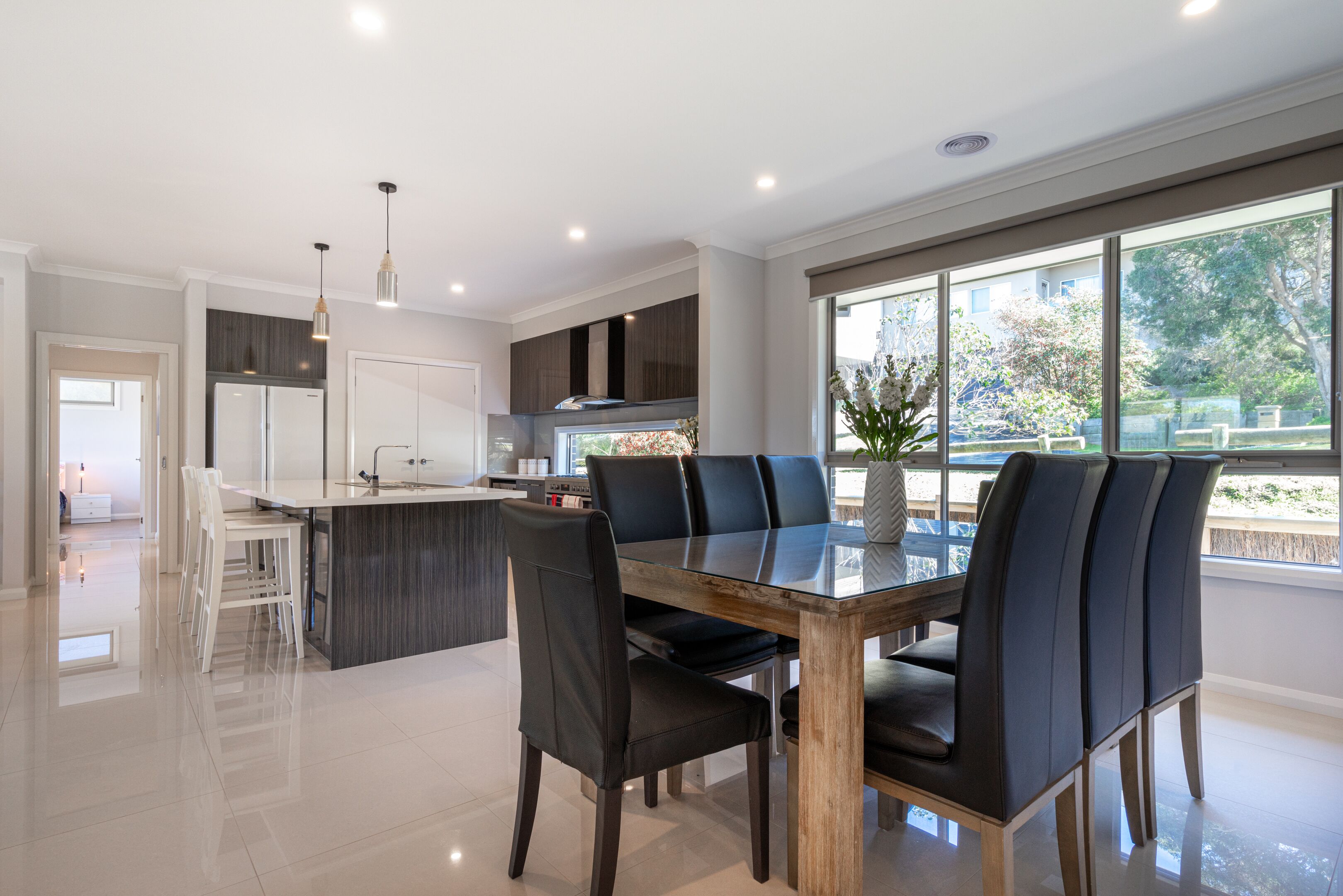 A modern kitchen with a central island, dark cabinetry, and a dining area with a glass table and chairs.