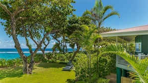 Un jardin luxuriant avec une piscine, un espace salon couvert et une vue sur l’océan.
