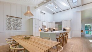 Une cuisine spacieuse avec des meubles blancs, une table à manger en bois et un grand îlot central doté de sièges.