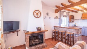 A living room with a fireplace, a television, and a kitchen area with a bar. - Cortijo El Gazpacho Periana by Ruralidays (Málaga)