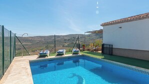 A swimming pool with three sun loungers, a small patio area with a table and chairs, and a view of the surrounding hills. - Cortijo El Gazpacho Periana by Ruralidays (Málaga)