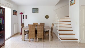 A dining area with wicker chairs and a table, a staircase with wooden steps, and a radiator on the wall.