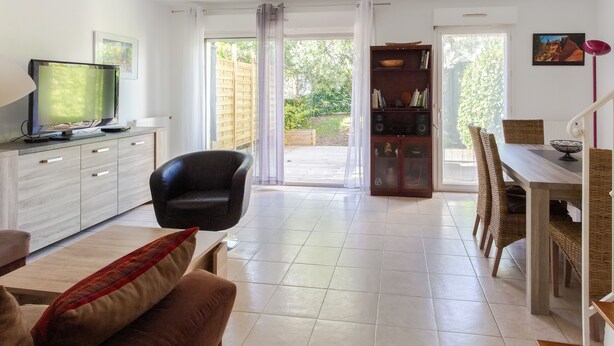 A modern living room with a flat-screen TV, a sofa, a dining table with chairs, and a bookshelf.