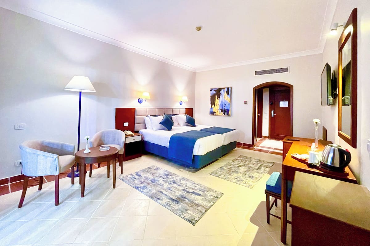 A hotel room with a bed, bedside tables, a desk, a chair, a lamp, and a painting on the wall.