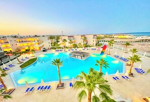 Ein Resort mit großem Schwimmbad, Liegestühlen, Palmen und Meerblick.