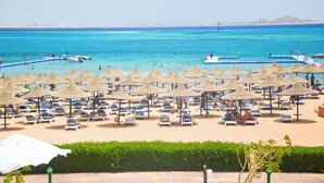 Una playa con tumbonas y sombrillas, una piscina y barcos en el agua.