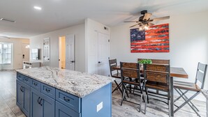 A modern kitchen with a granite countertop, blue cabinets, and a dining area with wooden chairs and a table.