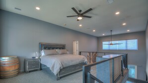 A bedroom with a bed, nightstands, a wooden barrel, and a balcony with a railing. - Cellar 74: New Modern Wine Casita w/Hot tub (Albuquerque)