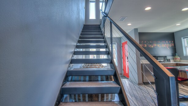 A modern staircase with a wooden finish, leading to a kitchen area with a red door and a black backsplash. - Cellar 74: New Modern Wine Casita w/Hot tub (Albuquerque)