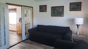 A living room with a dark-colored sofa, a small side table with a lamp, and three framed pictures on the wall.