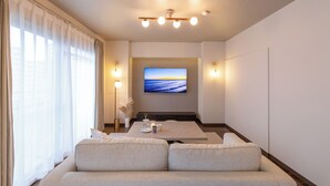Una habitación de hotel moderna con un ventanal grande, un televisor de pantalla plana montado en la pared, un sofá y una mesita con una bandeja de objetos.