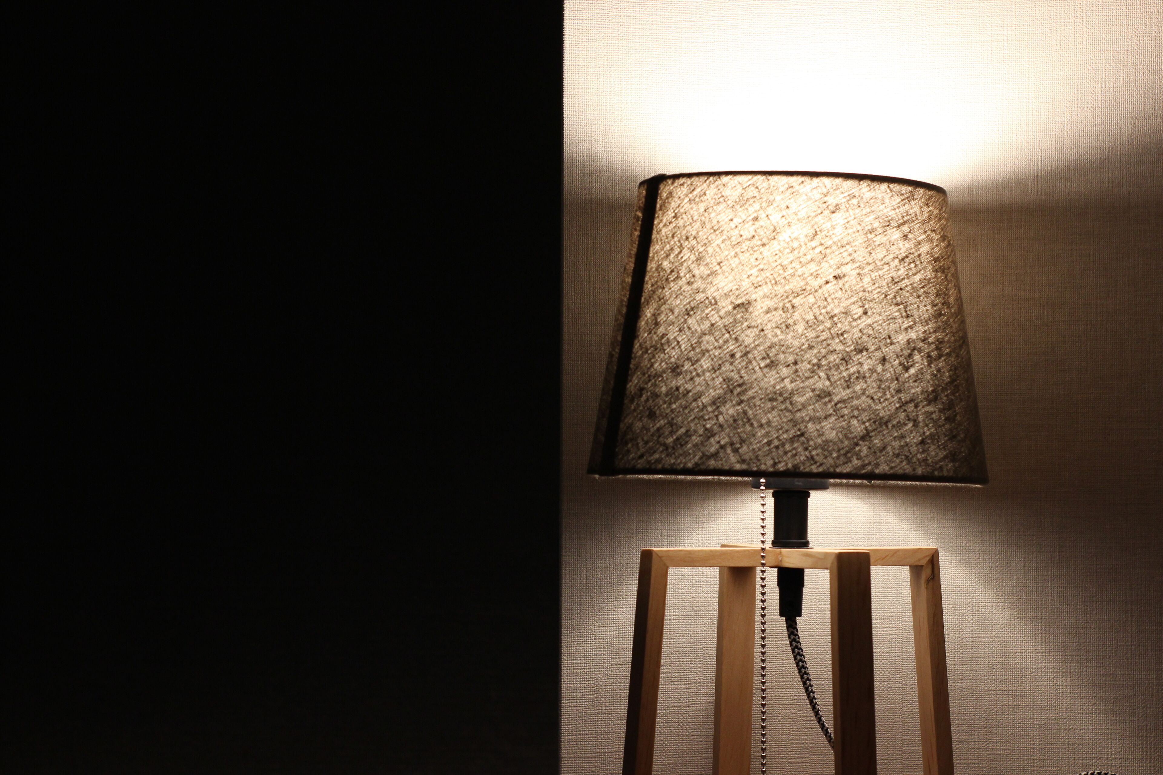 A lamp with a textured shade on a wooden stand against a textured wall.