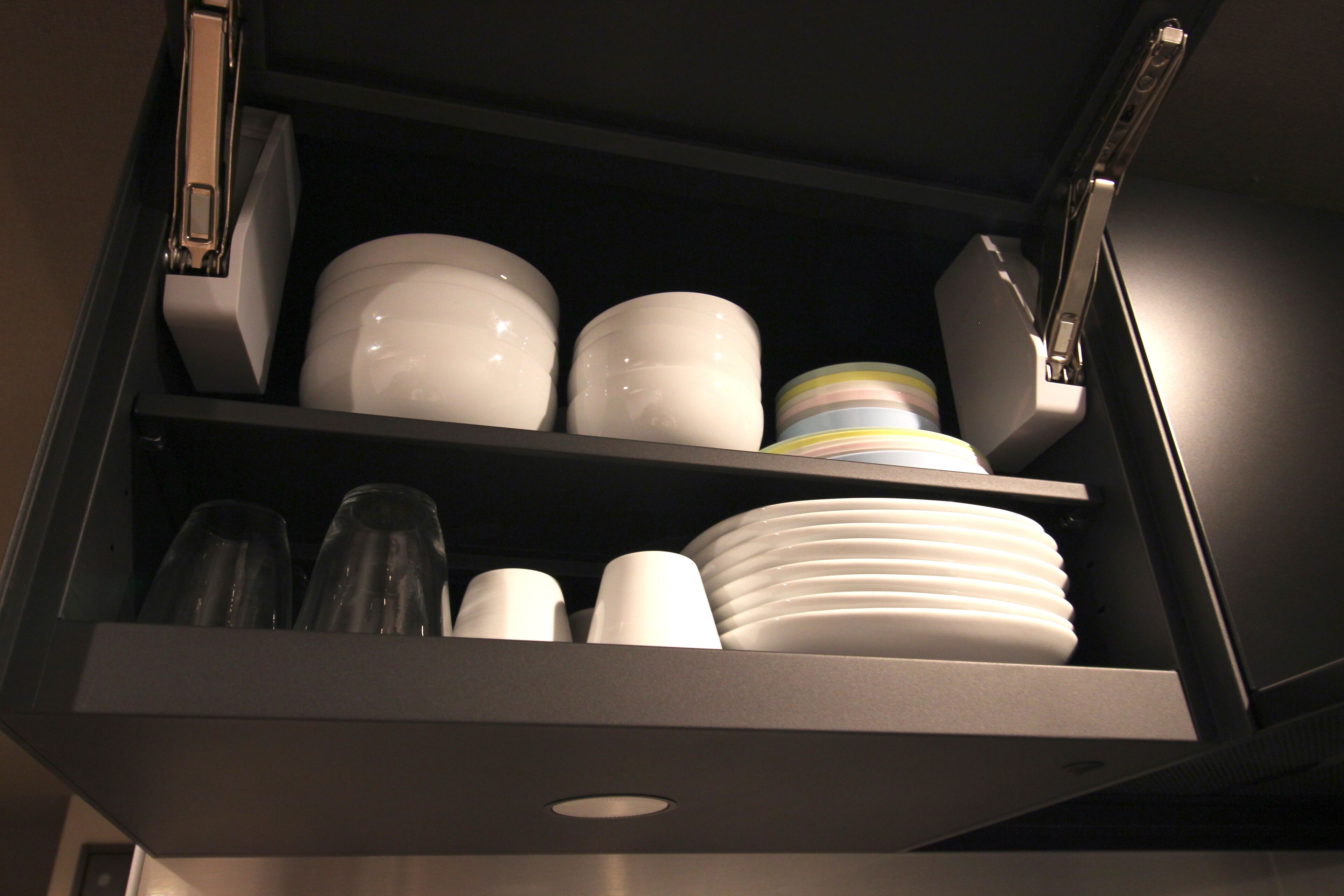 A kitchen cabinet with white plates, bowls, and clear glasses.