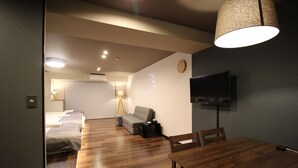 Una habitación de hotel moderna con suelo de madera, un sofá, una mesa de comedor y un televisor montado en la pared.