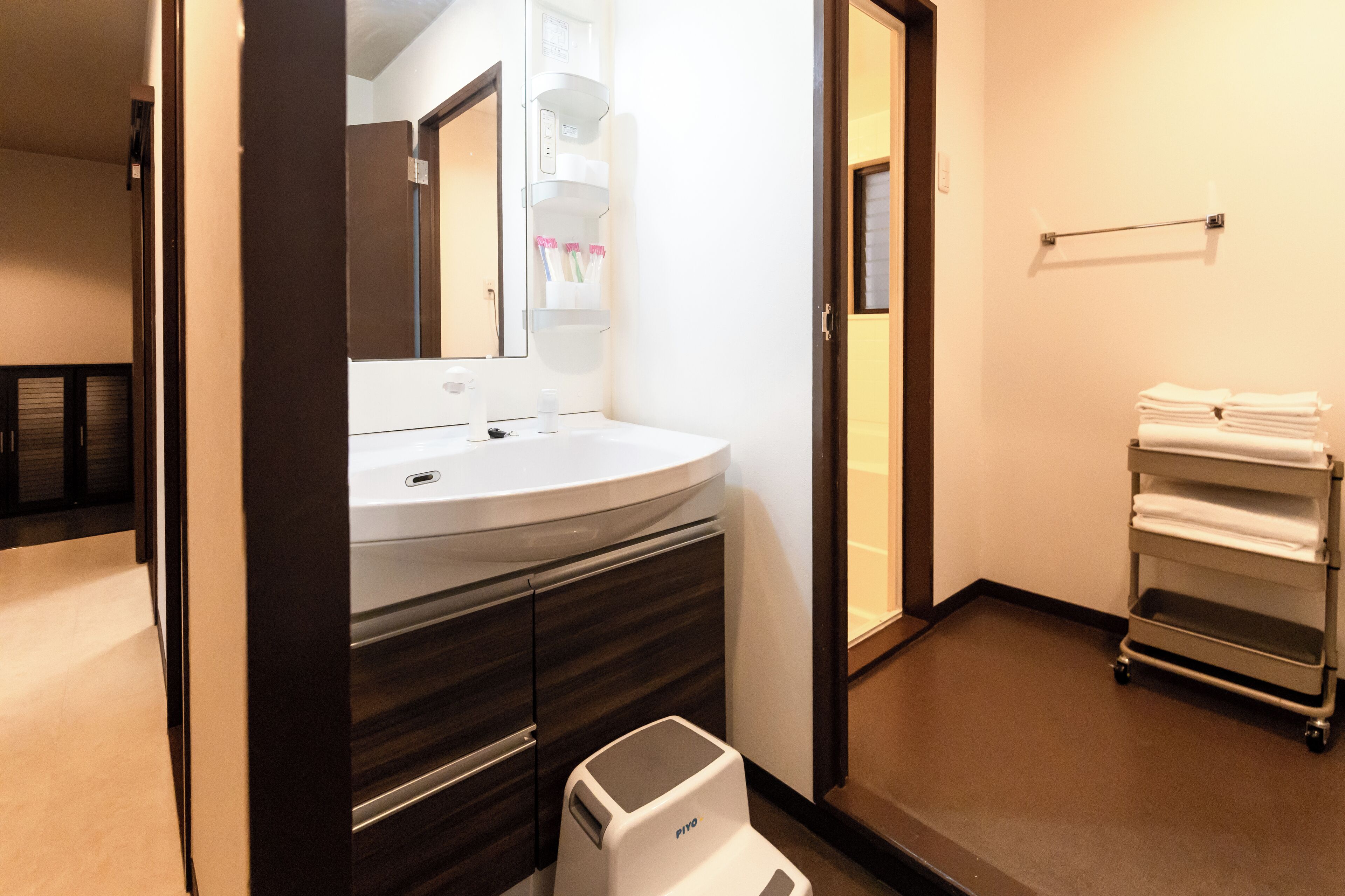 Un baño moderno con un lavabo blanco, tocador de madera oscura, un espejo y un perchero para toallas.
