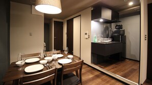 Un comedor moderno con una mesa de madera dispuesta para cuatro, una zona de cocina con microondas y estufa, y un espejo grande que refleja el espacio.