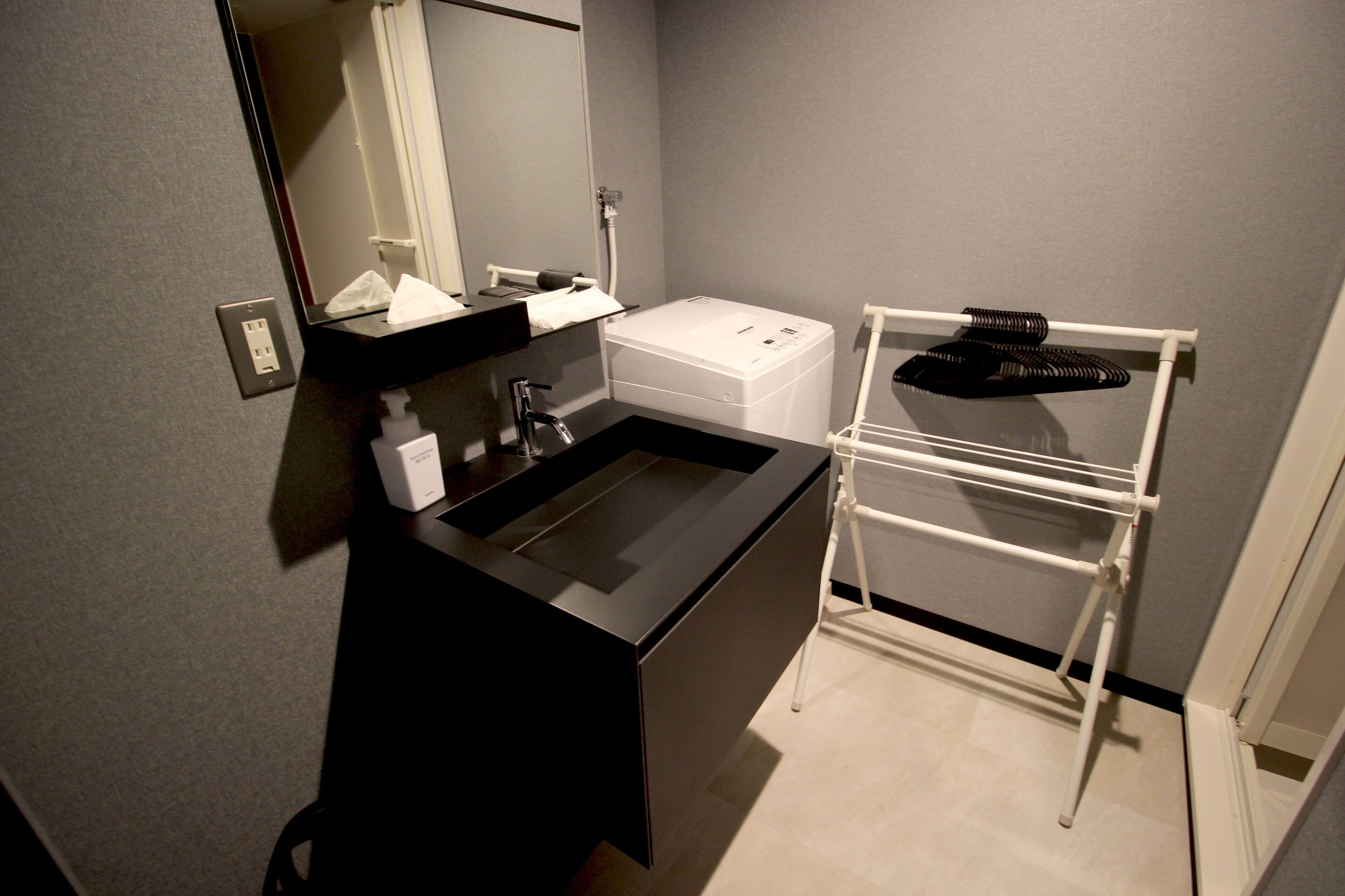 A modern bathroom with a black sink, a mirror, a white towel dispenser, and a white drying rack.