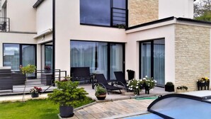 Una casa moderna de dos pisos con piscina, ventanas amplias y mobiliario exterior.