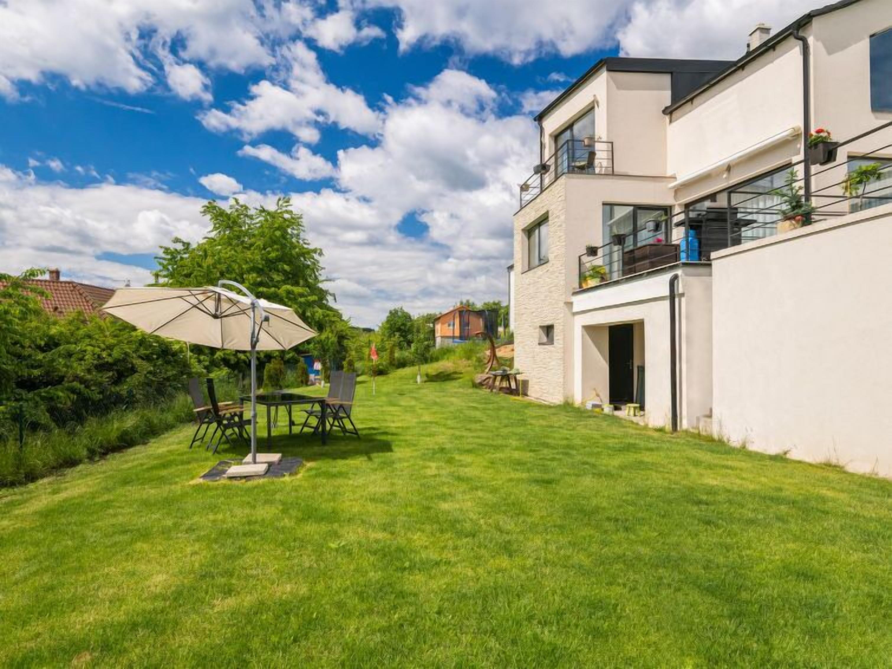 A modern two-story house with a well-maintained lawn, outdoor seating area, and a large umbrella.