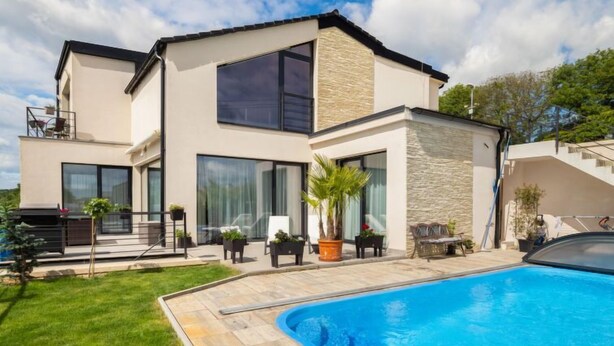 Una casa moderna de dos pisos con piscina, ventanas amplias y fachada de piedra.
