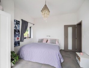 A bedroom with a bed, a window with curtains, a wall with photos, a door, and a plant. - Apartment Lány by Interhome (Lany)