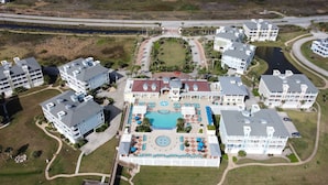 Luchtbeeld van een resort met meerdere gebouwen, een centraal zwembadgedeelte met ligbedden, en een omliggend landschap met een weg en een waterpartij.