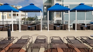 Een zwembadgedeelte met ligbedden en parasols, een witte omheining en een gebouw met een balkon op de achtergrond.