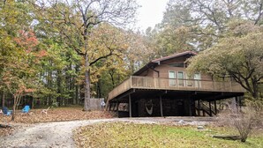 Een vakantiehuisje met een overdekte veranda, omringd door bomen en een pad bedekt met bladeren.