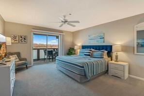 Ein Schlafzimmer mit einem großen Bett, einem Deckenventilator, einem Nachttisch, einer Kommode und Blick auf einen Balkon.