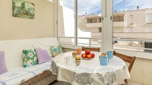 Ein Balkon mit einem weißen Frühstückstisch, einer Couch mit bunten Kissen und einem Bild an der Wand.