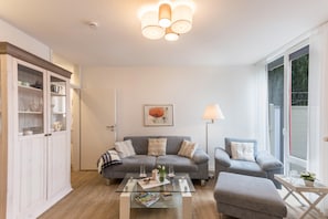 Un salon comprenant un canapé, un fauteuil, une table basse en verre et un meuble.