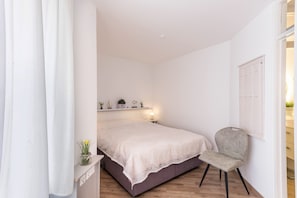Une chambre à coucher avec un lit, une chaise, une table de chevet et une étagère avec de petites plantes.