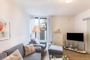Un salon avec un canapé, un pouf, une télévision et une lampe.