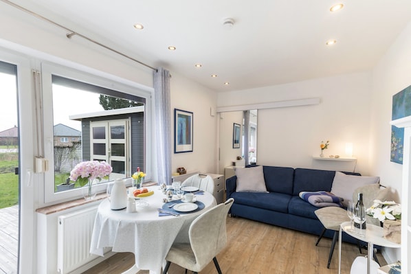 Un salon moderne avec un coin repas, un canapé bleu et une vue sur l’extérieur.