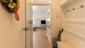Un couloir avec une porte vitrée donnant sur une pièce, un mur blanc orné d’une guirlande décorative et un meuble blanc muni de crochets.