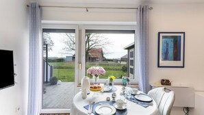 Un coin repas avec une table dressée pour quatre personnes, une vue sur l’extérieur et un tableau accroché au mur.