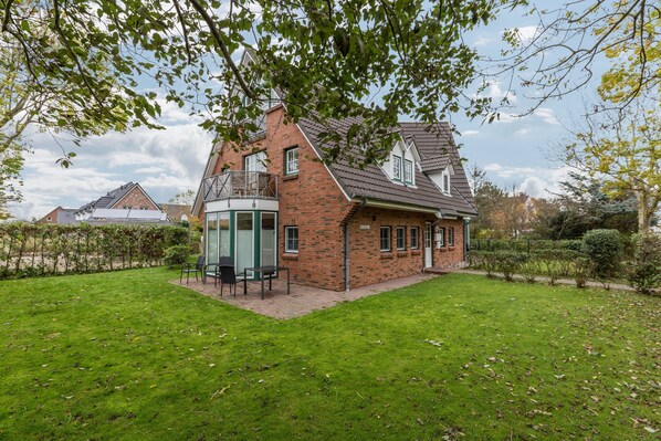 Une maison à deux étages avec une façade en briques, un petit balcon et une pelouse verdoyante.
