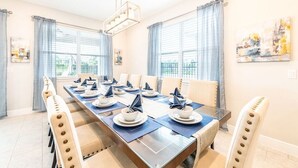 Comedor con una larga mesa dispuesta para una comida, sillas de diseño único e iluminación colgante moderna.