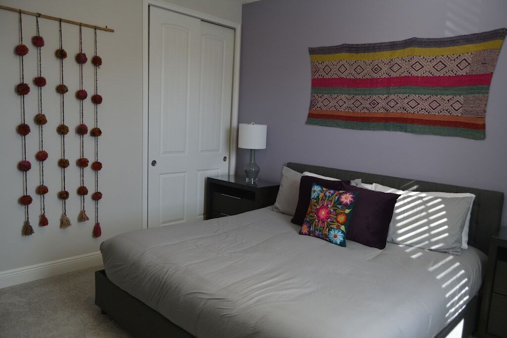 A bedroom with a bed, a nightstand, a lamp, a wall hanging, and a door.
