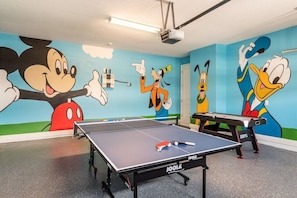 Une pièce équipée de deux tables de ping-pong, d’un projecteur et d’une fresque murale représentant des personnages de dessins animés.